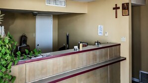 A reception desk with a beige counter, a red accent, and a cross on the wall. - OYO Hotel Guymon OK US-54 (Guymon)