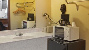 A compact bathroom with a white sink, a mirror, a black refrigerator, and a coffee machine. - OYO Hotel Guymon OK US-54 (Guymon)
