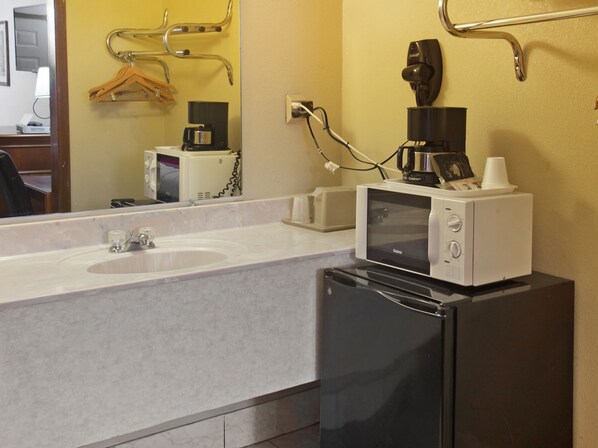 Une petite salle de bain avec un lavabo blanc, un miroir, un réfrigérateur noir et une machine à café.