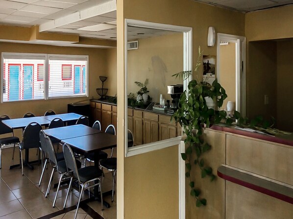 A dining area with tables and chairs, a kitchen area with cabinets and appliances, and a view of the outside through a window with blinds. - OYO Hotel Guymon OK US-54 (Guymon)