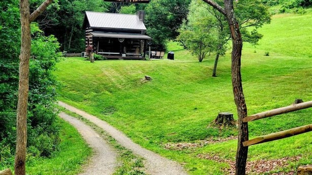 Ein rustikaler hölzerner Bogen führt zu einer Hütte mit der Aufschrift "The Brock Cottage" inmitten einer üppigen grünen Landschaft.