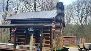 Eine rustikale Holzhütte mit einem Metalldach, einem Steinkamin und einer Terrasse mit Gartenmöbeln.
