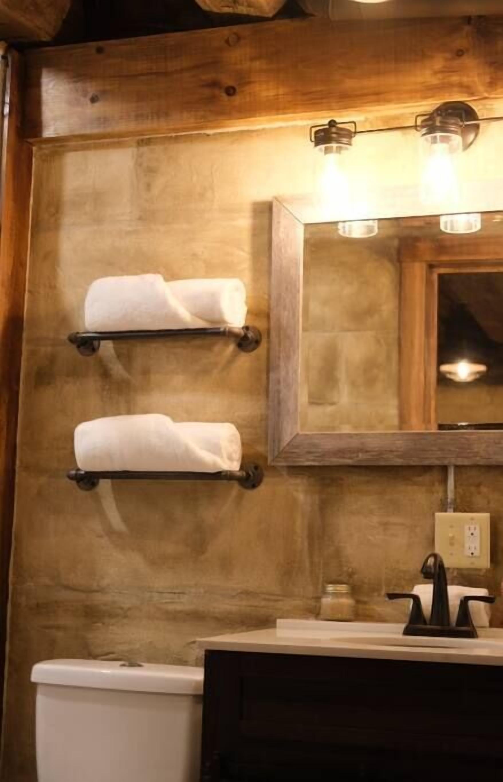 A bathroom with wooden walls, a white toilet, a dark sink, and two towel racks with white towels.