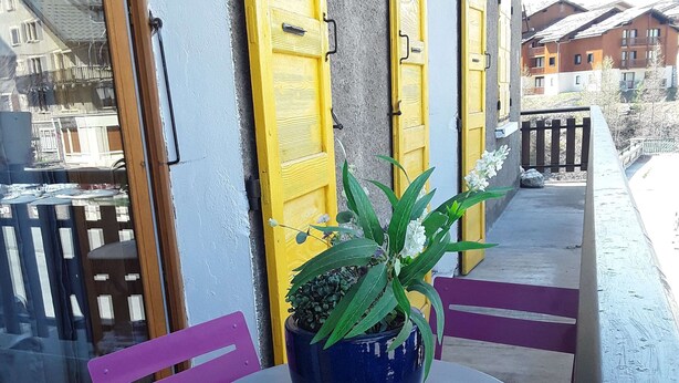 A balcony with a round table and two chairs, a potted plant, and yellow doors. - Termignon Val cenis Vanoise (Termignon Val cenis)
