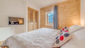 A bedroom with a bed, wooden walls, a window with curtains, and a small shelf with a mirror. - 50m from ski slopes, 9th floor, balcony, parking, tv, ski locker, 52m², Champagny-en-Vanoise (Champagny-en-Vanoise)