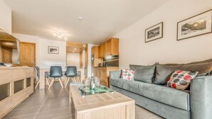 A modern living room with a grey sofa, wooden coffee table, and a dining area with a wooden table and chairs. - 50m from ski slopes, 9th floor, balcony, parking, tv, ski locker, 52m², Champagny-en-Vanoise (Champagny-en-Vanoise)
