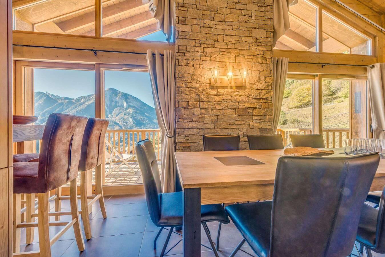 A dining area with a stone wall, wooden ceiling, and large windows offering mountain views.