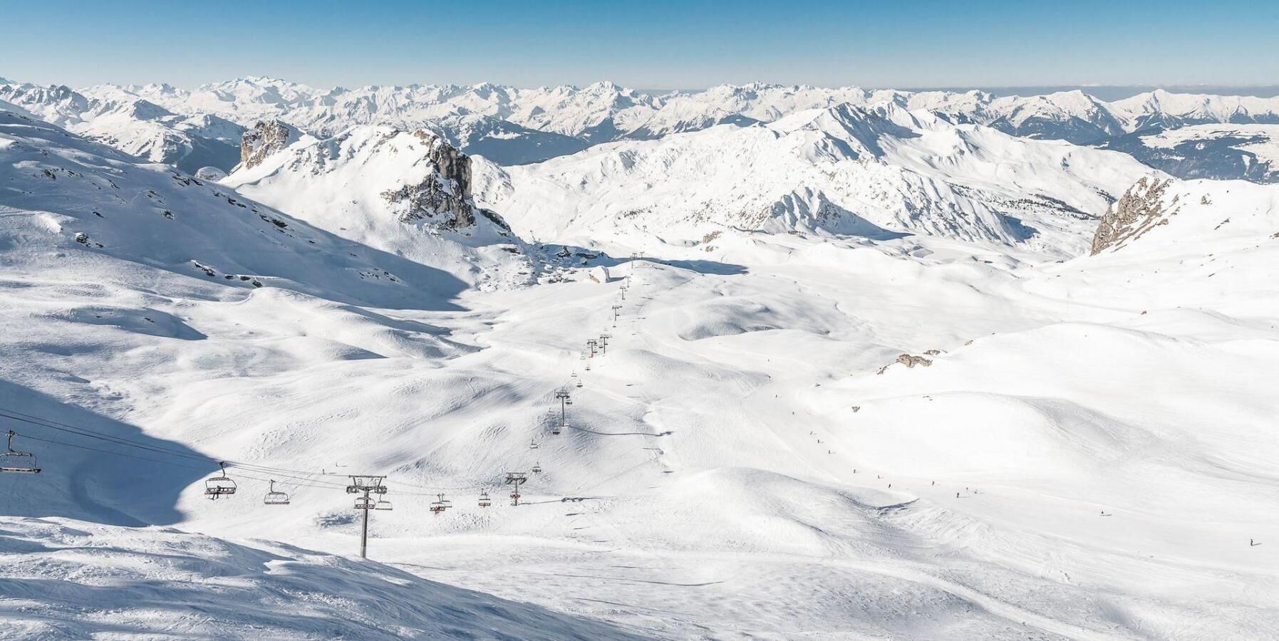 Paisaje montañoso cubierto de nieve con telesillas y cielo despejado.