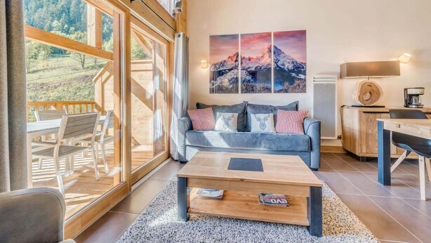 Un salon moderne avec une grande fenêtre, un canapé, une table basse et un tableau représentant une montagne.