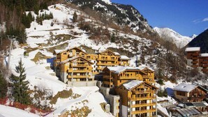 Un chalet de montagne composé de plusieurs bâtiments en bois, avec des pistes de ski et un ciel dégagé.