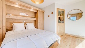Une chambre à coucher avec une tête de lit en bois, un lit avec une literie blanche, un miroir rond et une porte en bois.