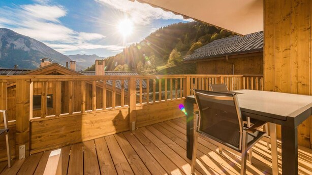 Une terrasse en bois avec une table et des chaises, offrant une vue sur un paysage montagneux sous un ciel dégagé.