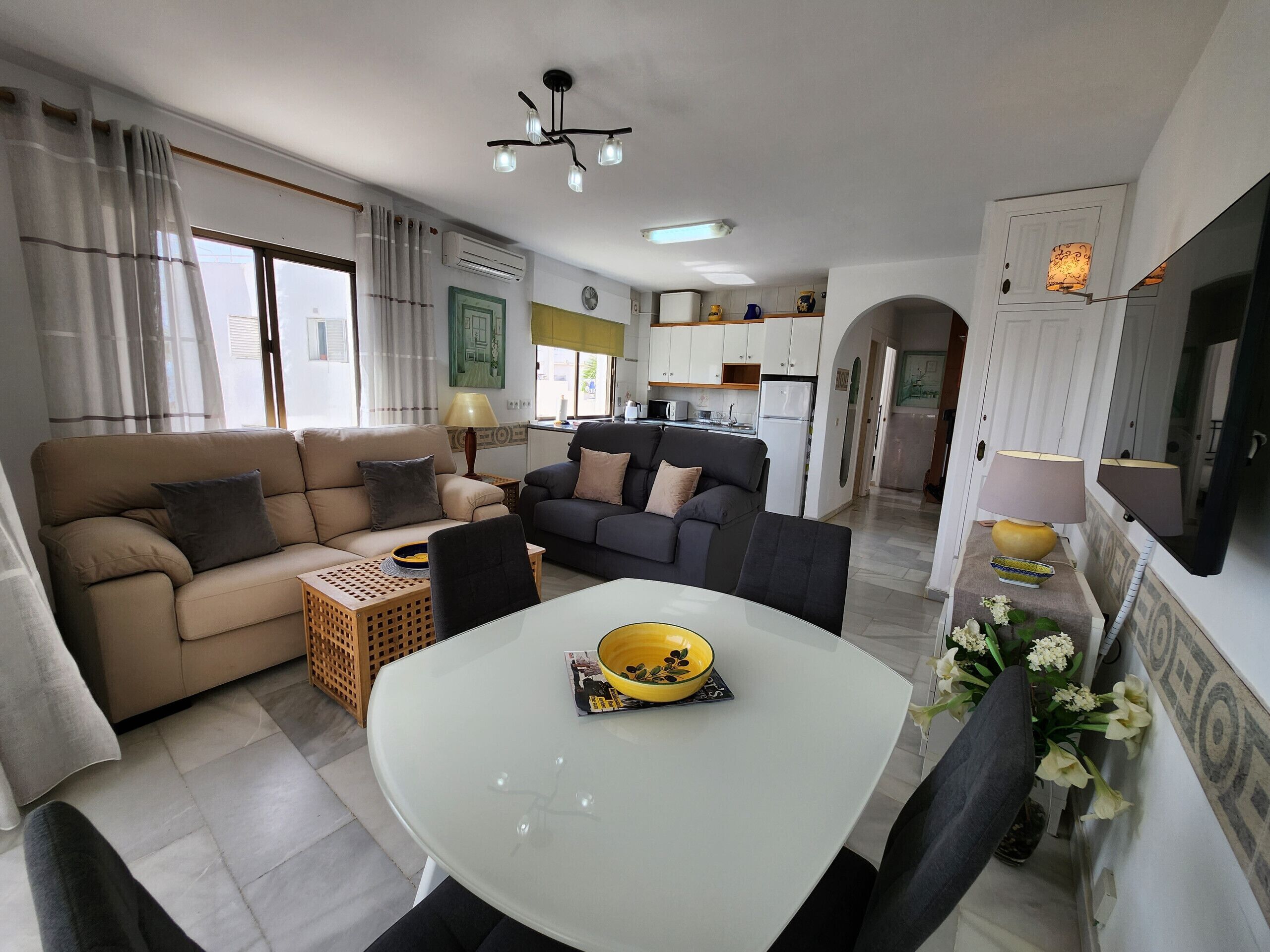 Ein modernes Wohnzimmer mit einer Couch, einem Esstisch mit einer Schüssel und einer Küche im Hintergrund.
