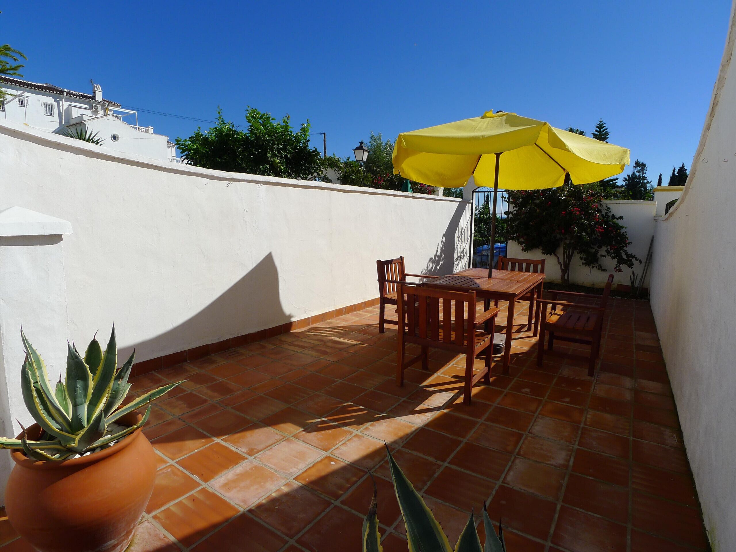 A patio with a table and chairs, a yellow umbrella, and a potted plant.