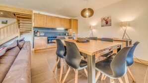 A modern kitchen with wooden cabinets, a dining area with a wooden table and black chairs, and a staircase leading to a loft bedroom. - 100m from resort center, 12nd floor, balcony, parking, tv, ski locker, 90m², Champagny-en-Vanoise (Champagny-en-Vanoise)