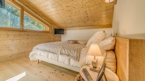 A bedroom with a wooden ceiling, a bed with a beige blanket, a mounted TV, and a lamp on a bedside table. - 100m from resort center, 12nd floor, balcony, parking, tv, ski locker, 90m², Champagny-en-Vanoise (Champagny-en-Vanoise)