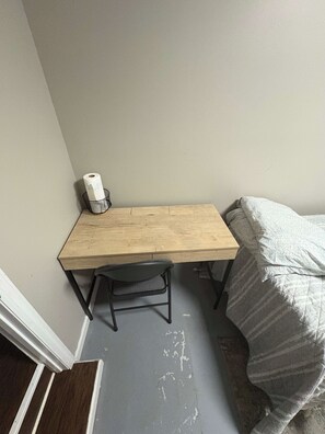 Pieni huone, jossa on puinen työpöytä, tuoli ja sängyllä kuvioitu peitto.