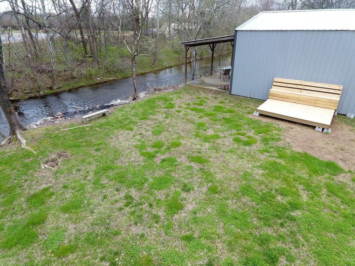 Une cour arrière verdoyante avec un banc en bois, un abri de jardin et une rivière.