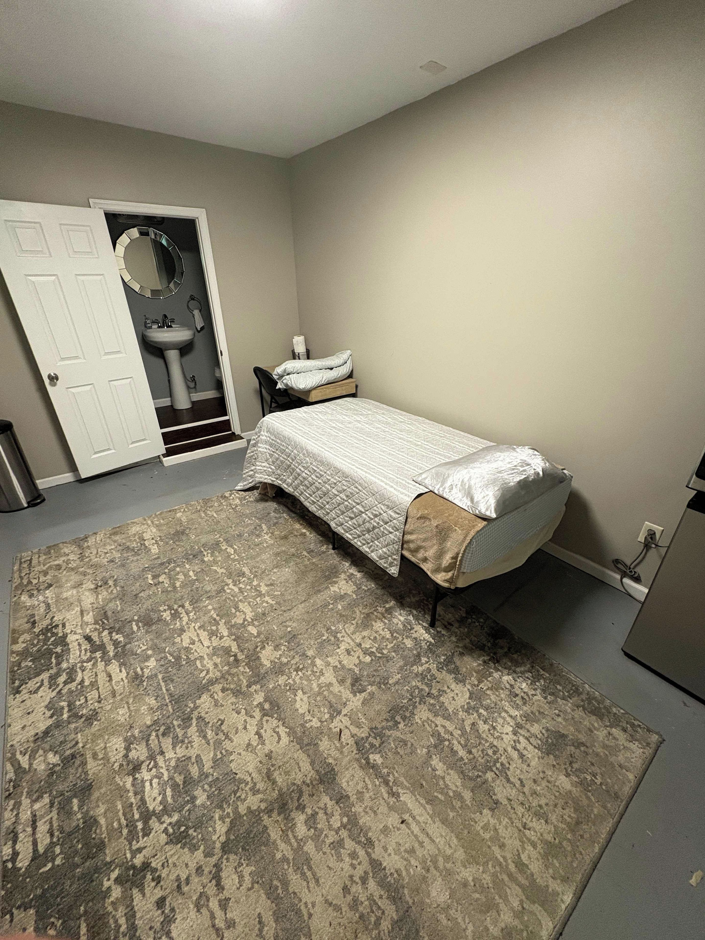 A bedroom with a bed, a rug, a sink, and a door.