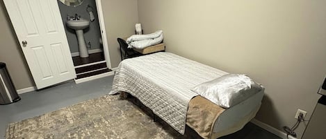A bedroom with a bed, a rug, a sink, and a door.