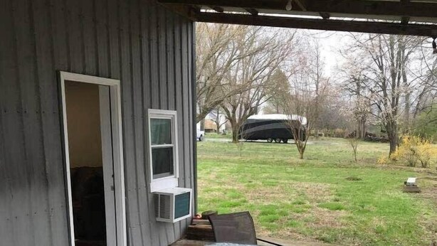 A covered patio with a glass table and two chairs, an air conditioning unit, and a view of a grassy yard with trees and a parked vehicle. - Delightful Guest Room Close to Hendersonville’s Downtown (Hendersonville)