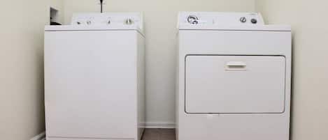 Een wasserette met twee witte wasmachines, een wandcontactdoos en een betegelde vloer.