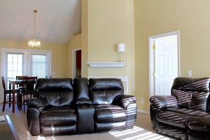A living room with a dark leather sofa, a dining area with a table and chairs, and a white door. - Enjoy a Fenced Yard Just 20 Minutes from Nashville (Goodlettsville)