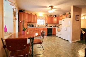 Une cuisine avec des meubles de rangement en bois, une table à manger avec des chaises, un ventilateur de plafond et un réfrigérateur.