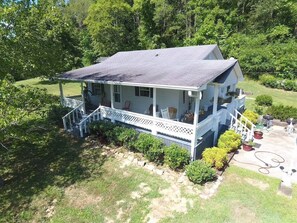 A two-story house with a porch, surrounded by greenery.