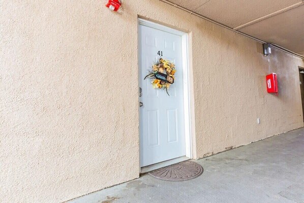 A building entrance with a white door marked with the number 41, a red fire alarm box, and a doormat.
