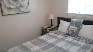 A bedroom with a bed, a nightstand, a lamp, and a large floral painting on the wall. - Cozy 1 BR efficiency apt close to TTU and downtown (Cookeville)