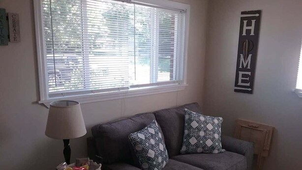 A living room with a grey sofa, patterned cushions, a lamp on a side table, and a 'HOME' sign on the wall. - Cozy 1 BR efficiency apt close to TTU and downtown (Cookeville)
