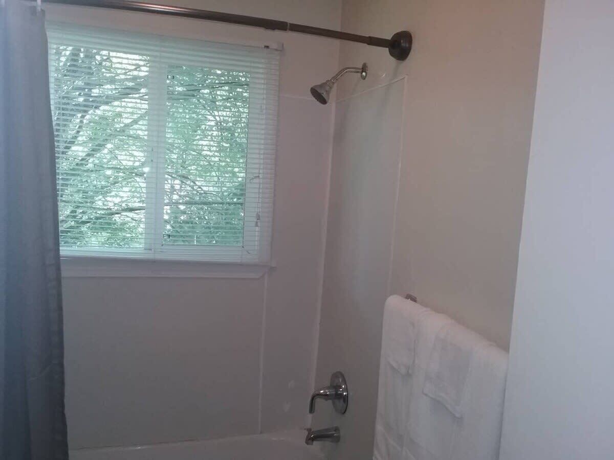 Une salle de bain avec une douche, une fenêtre avec des stores et un porte-serviettes.