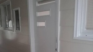 En hall med en vit dörr, en välkomstmatta och ett litet fönster med utsikt.