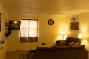 Ein Wohnzimmer mit einer Couch, einem flachbildfernseher an der Wand, einer Uhr und einem Gemälde.
