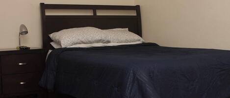 Una cama bien hecha con un edredón azul oscuro y una almohada blanca con estampado floral.