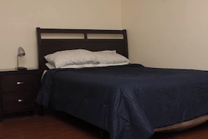 Ein Einzelbett mit dunklem Kopfteil, ein Nachttisch mit Lampe und eine Kommode.