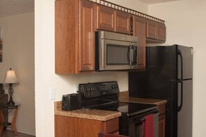Una cocina compacta con armarios de madera, un microondas de acero inoxidable, un refrigerador negro y una estufa.