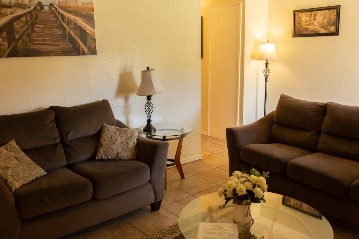 A living room with two sofas, a glass coffee table with flowers, a lamp, and a painting on the wall.