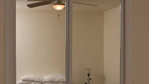 Quarto com cama, ventoinha no teto e mesa de cabeceira com luminária.