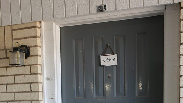 Una puerta gris con un letrero que dice 'welcome', una cerradura electrónica y una lámpara de pared.