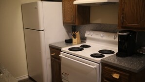 Una cocina con refrigerador, estufa y horno blancos, armarios de madera y encimera de granito.