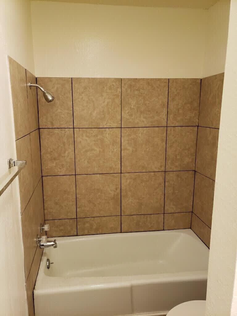 A bathroom with a bathtub, a showerhead, and a toilet.