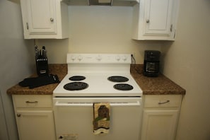 A kitchen with a white stove, four burners, and a coffee maker on the countertop. - Cozy Apartment Just Minutes from Fort Sill (Lawton)