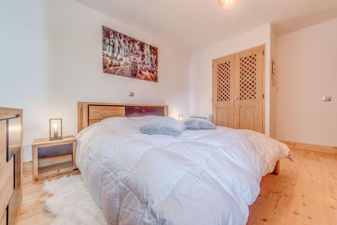 Un dormitorio con una cama grande, cabecera de madera, una mesita de noche con lámpara, un tapete blanco y un armario de madera.