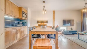 Una cocina moderna con armarios de madera, horno empotrado y comedor con mesa y sillas de madera.