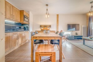A modern kitchen with wooden cabinets, a built-in oven, and a dining area with a wooden table and chairs.