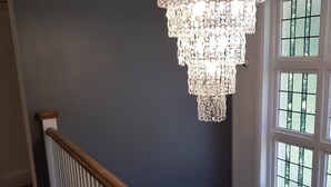 Een trap met een witte leuning en een houten handrailing, die leidt naar een kamer met een groot raam en een kroonluchter.