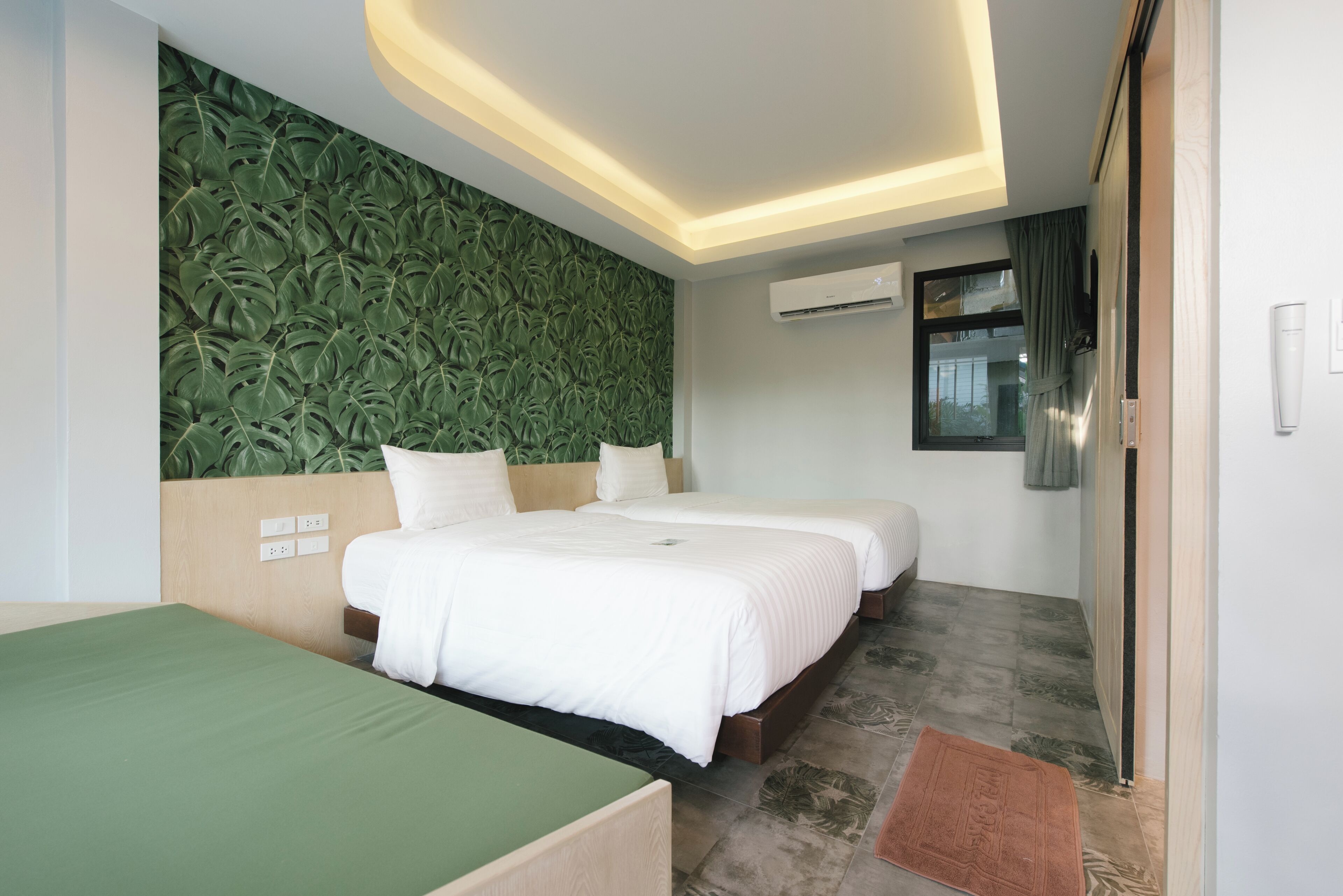 A hotel room with two beds, a green sofa, a patterned wall, and an air conditioning unit.