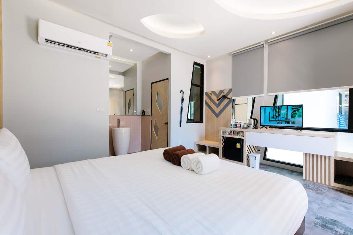 Una habitación de hotel moderna con una cama grande, televisión de pantalla plana, escritorio con silla y baño con espejo y lavamanos.